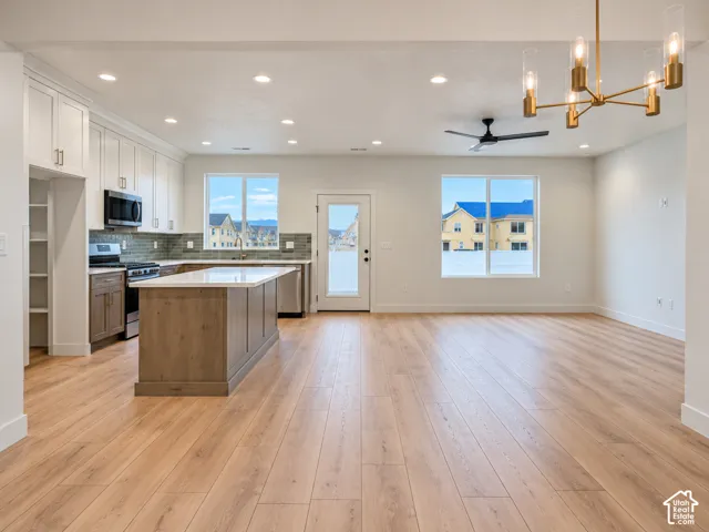 Kitchen featuring wood-finish flooring, a central island with a stone countertop, white upper cabinetry, tiled backsplash, and recessed lighting