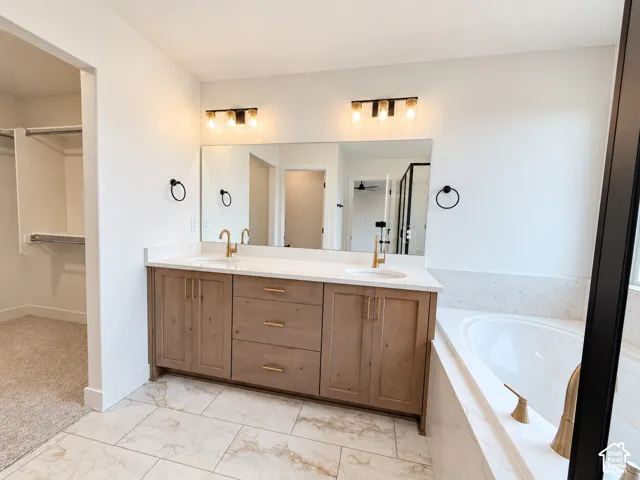 Dual-sink vanity featuring warm wood-finish cabinetry, quartz countertops, brushed-gold fixtures, and a large wall-mounted mirror