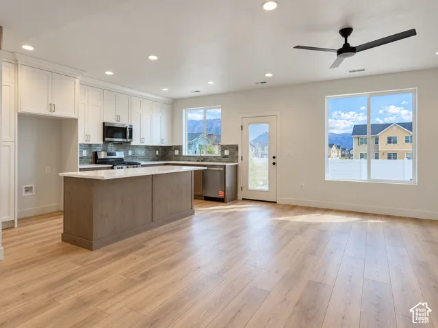 Kitchen featuring a central island with a solid surface countertop, white shaker-style cabinetry, stainless steel appliances, a tiled backsplash, and wood-finish flooring