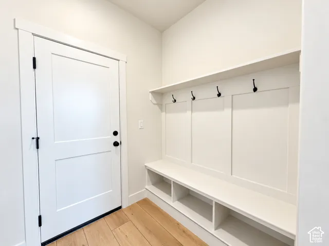 Built-in mudroom bench with integrated storage cubbies, white paneling, overhead shelf, and matte black wall-mounted hooks, complemented by wood-finish flooring and a shaker-style door with matte black hardware
