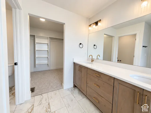 Double vanity featuring wood-finish cabinetry, white solid-surface countertops, integrated dual sinks, and matte gold-tone hardware