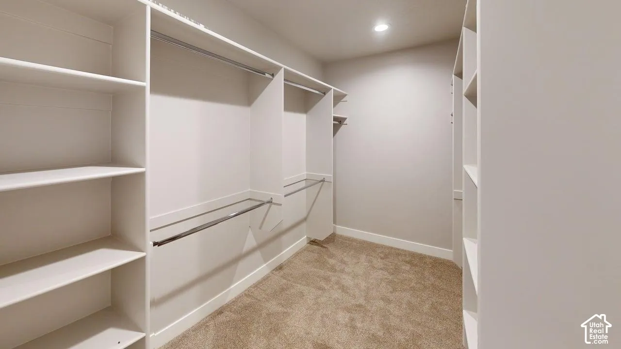 Custom walk-in closet featuring extensive built-in white shelving, dual-level metal hanging rods, recessed ceiling lighting, and wall-to-wall carpeting