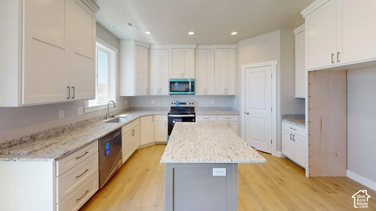 Kitchen featuring white cabinetry, stone-surface countertops, central island, wood-finish flooring, and stainless steel appliances