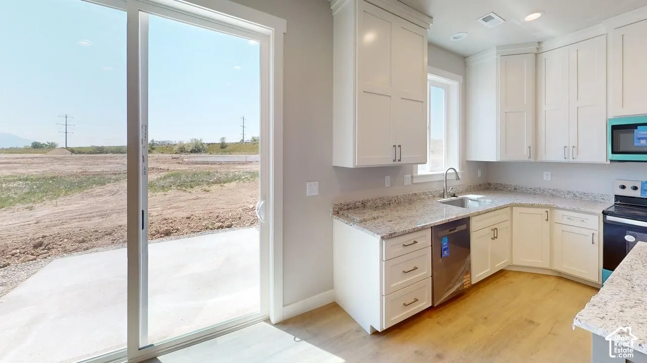 Kitchen featuring white shaker-style cabinetry, stone-finish countertops, stainless steel undermount sink, wood-finish flooring, and a large sliding glass door