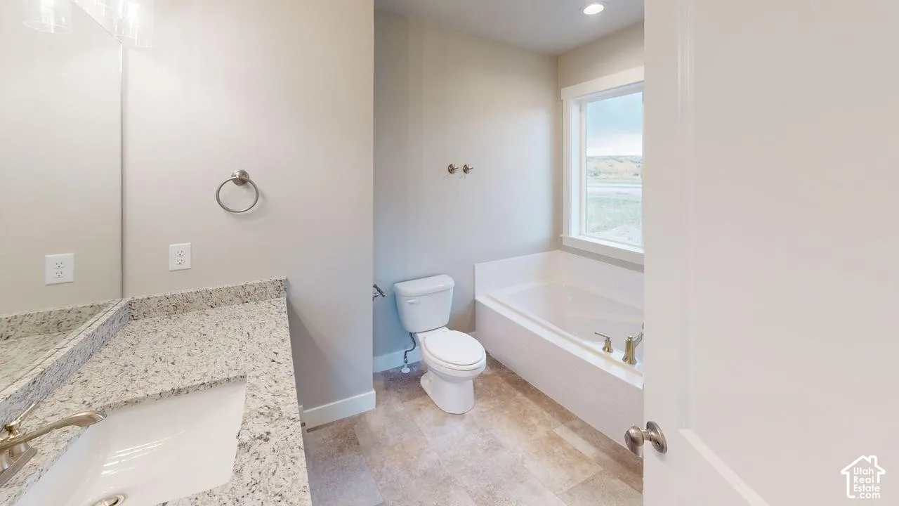 Bathroom featuring a stone-composite countertop, undermount sink, built-in soaking tub with a deck mount faucet, and tile flooring
