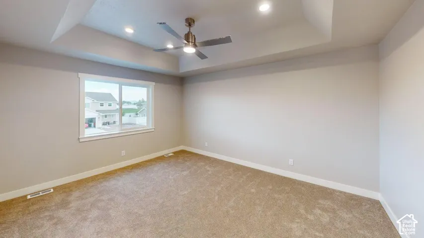 Room featuring a tray ceiling, neutral wall coloring, carpeting, a ceiling fan with integrated lighting, and recessed overhead lighting