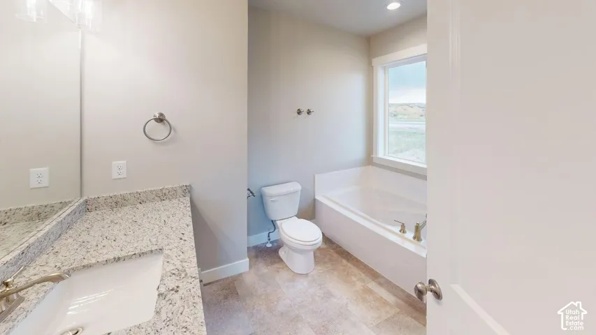 Bathroom featuring a stone-composite countertop, undermount sink, built-in soaking tub with a deck mount faucet, and tile flooring