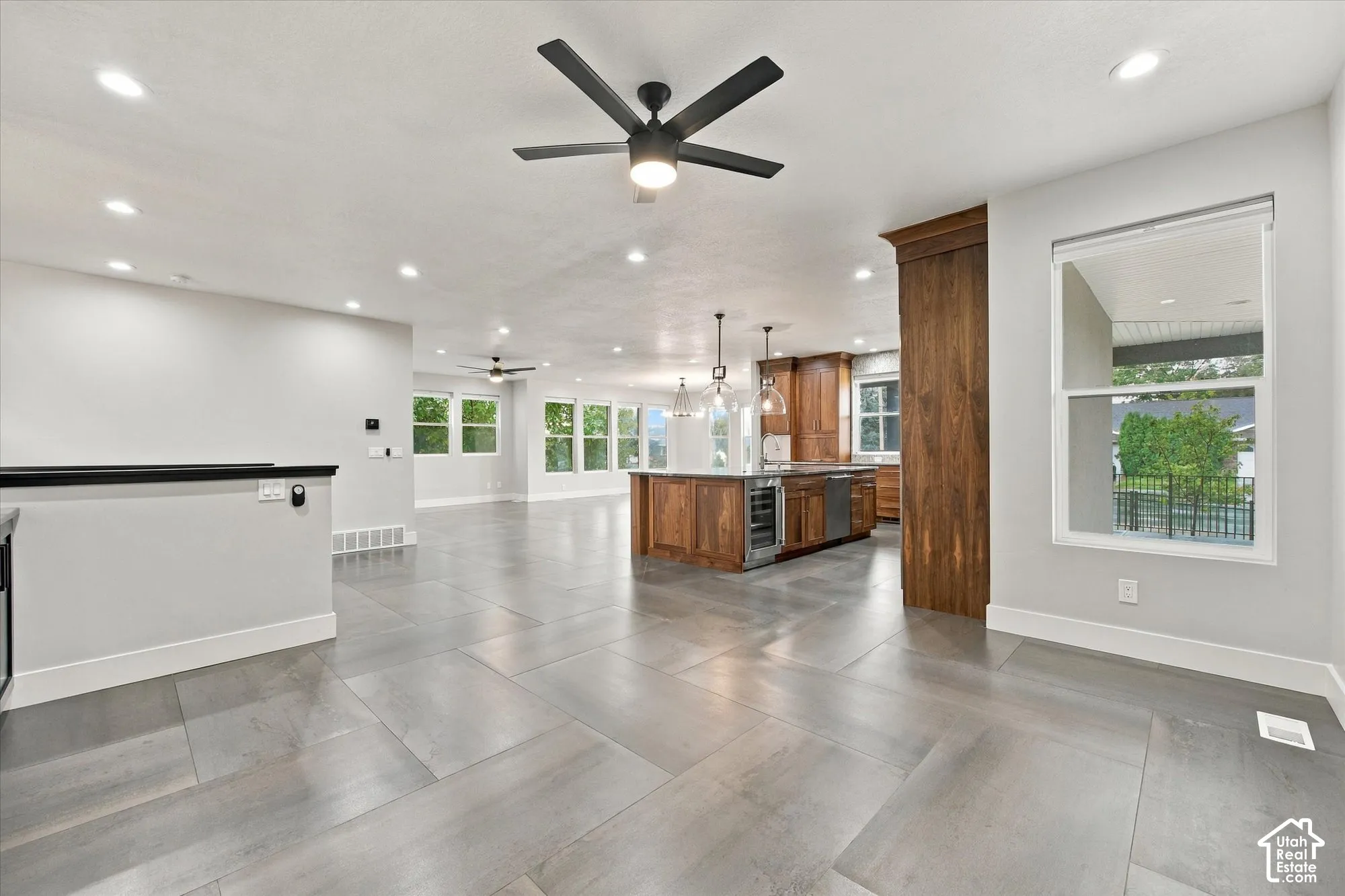 Open-concept interior featuring large-format tile flooring, recessed ceiling lighting, a central kitchen island with built-in cabinetry, and matte black ceiling fans