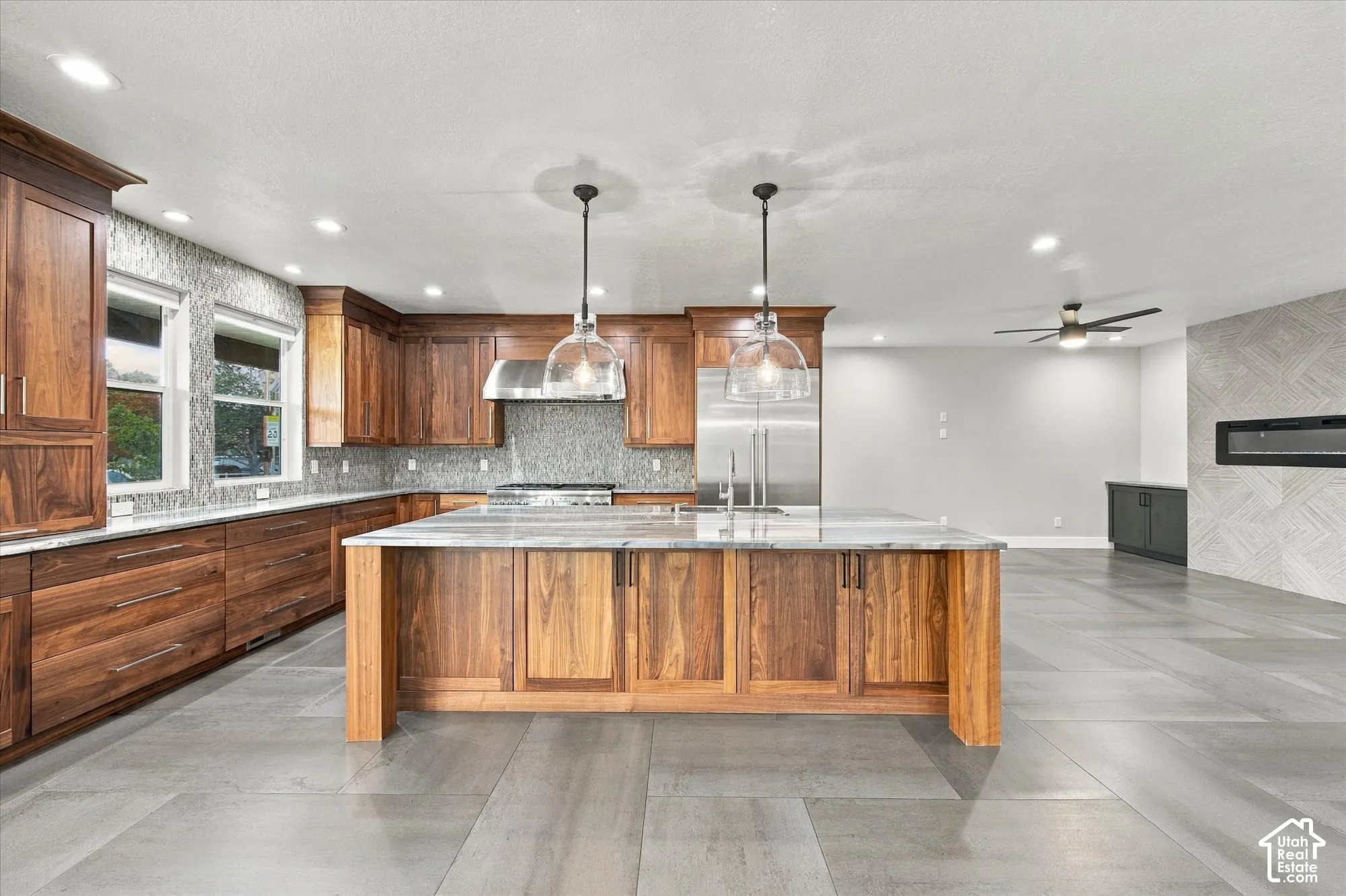 Kitchen featuring stained wood cabinetry, stone countertops, large center island with dual pendant lighting, stainless steel appliances, and large-format tile flooring