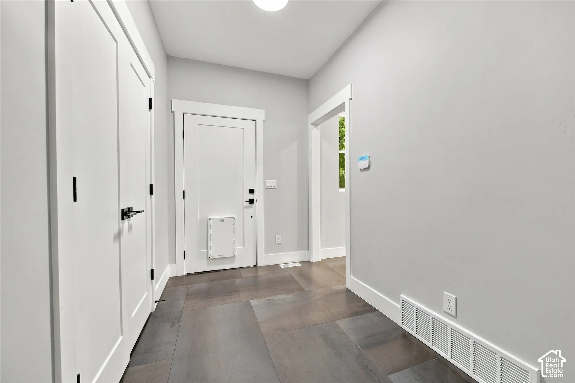 Neutral-toned interior space featuring large-format ceramic tile flooring, clean-lined white door casings, solid-core interior doors with matte black hardware, and an integrated wall-mounted pet door
