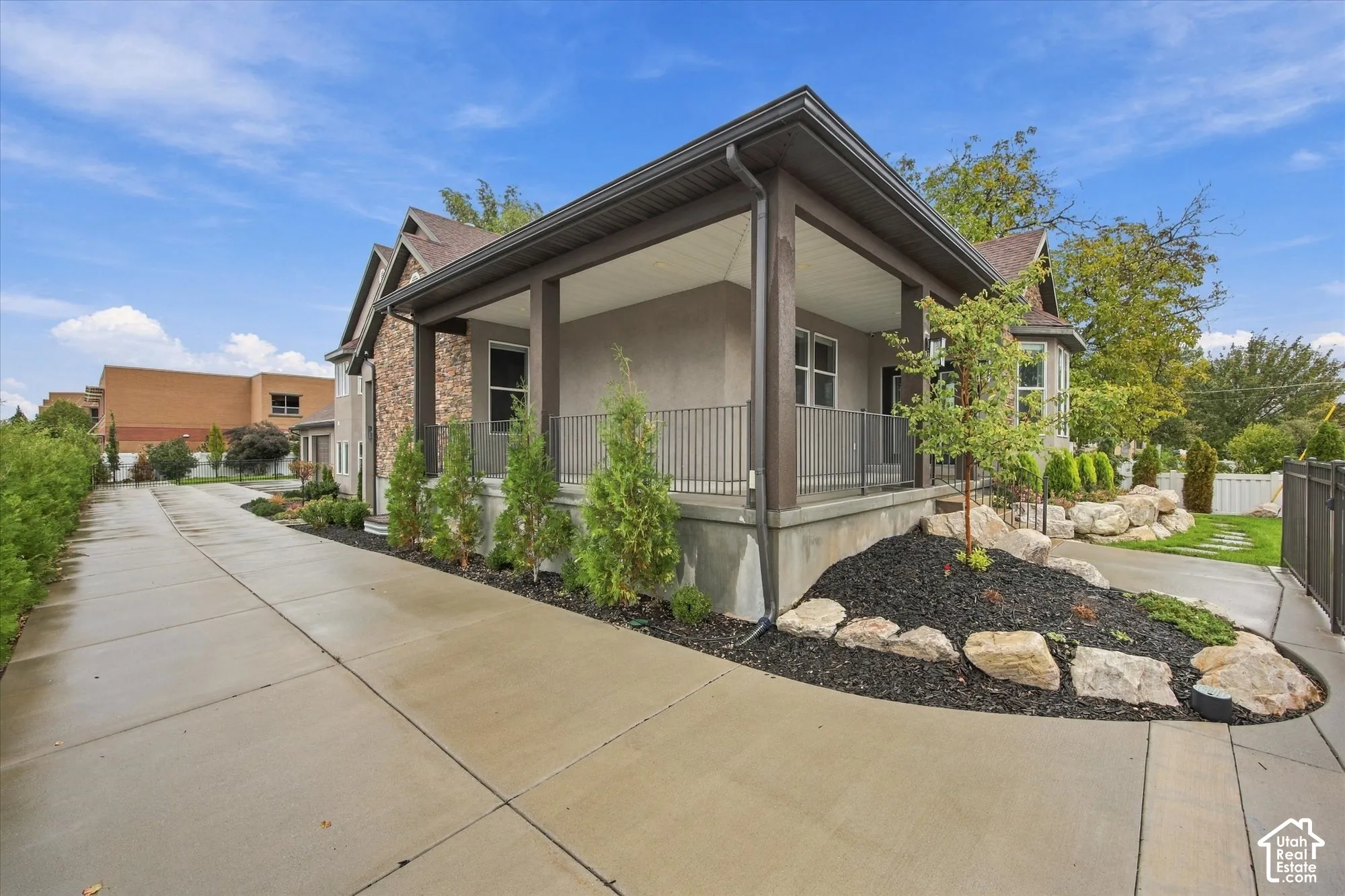 Covered porch with metal railing, stone veneer accents, concrete driveway, and landscaped rock garden beds