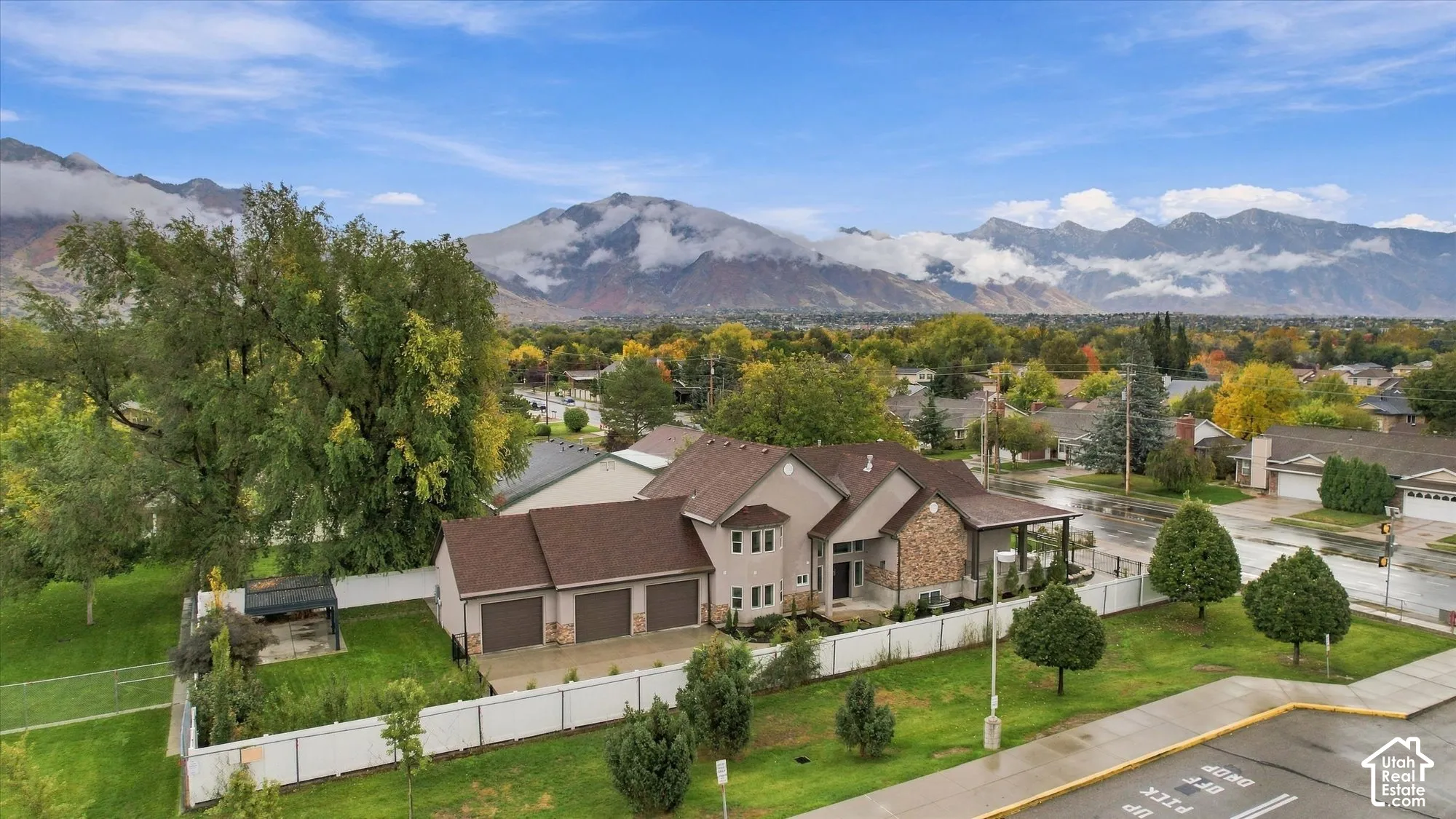 Multi-level residence featuring a stone and stucco exterior, an attached three-car garage, a perimeter vinyl fence, and a mountain backdrop