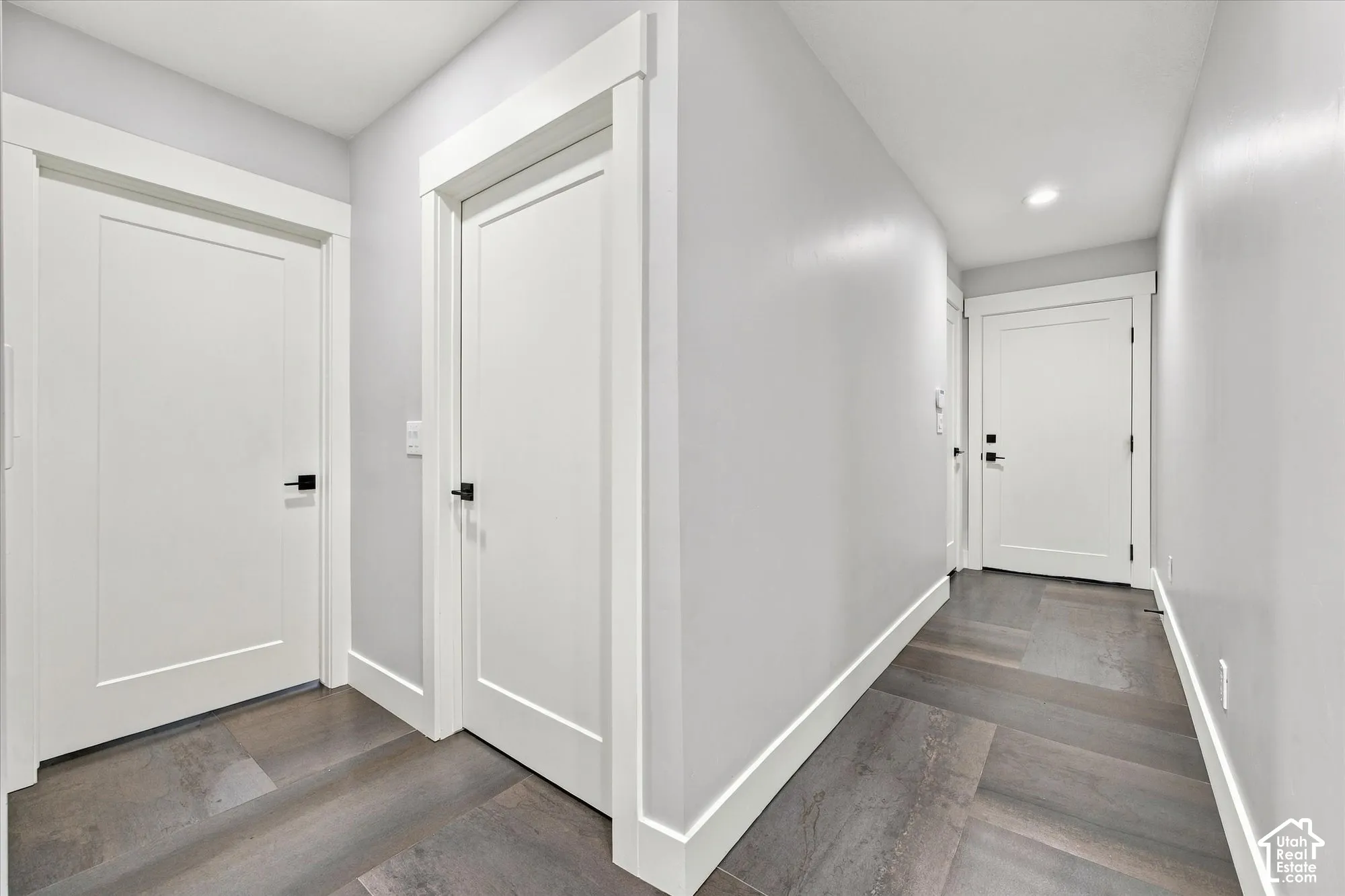 Hallway featuring wood-finish flooring, white shaker-style doors, matte black hardware, and crisp white trim