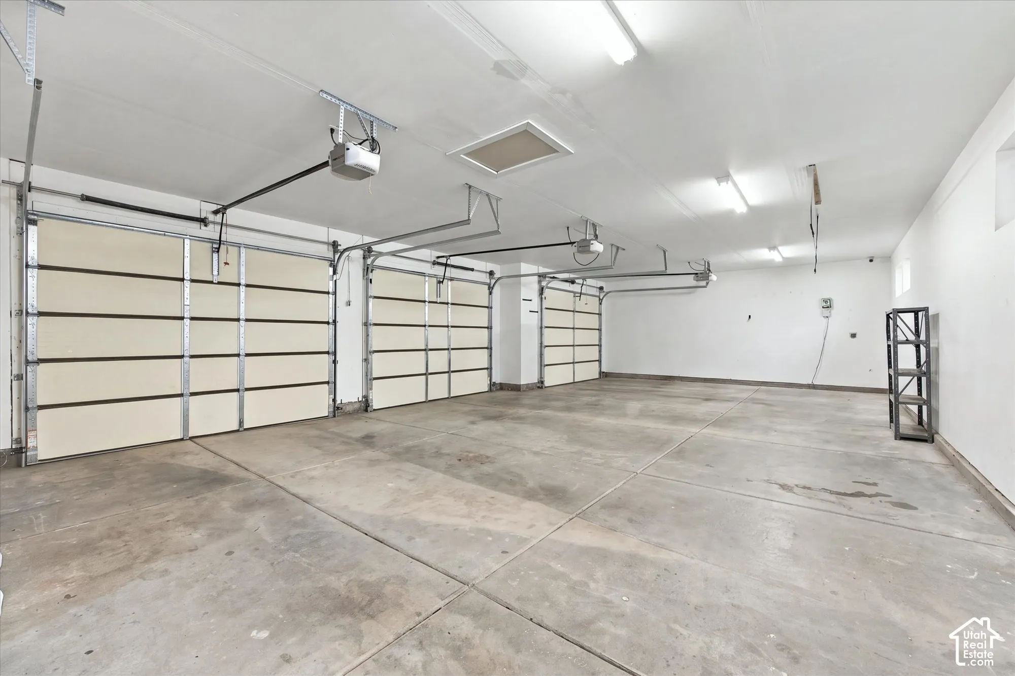 Three-car garage featuring finished walls, concrete flooring, linear fluorescent lighting, and automatic door openers