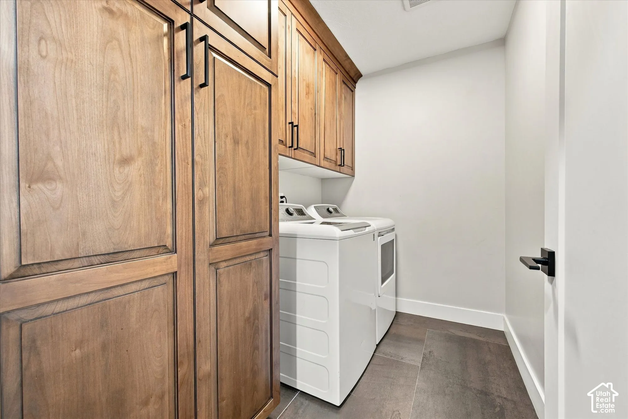 Laundry area featuring wood-finish cabinetry, matte black hardware, and wood-finish flooring