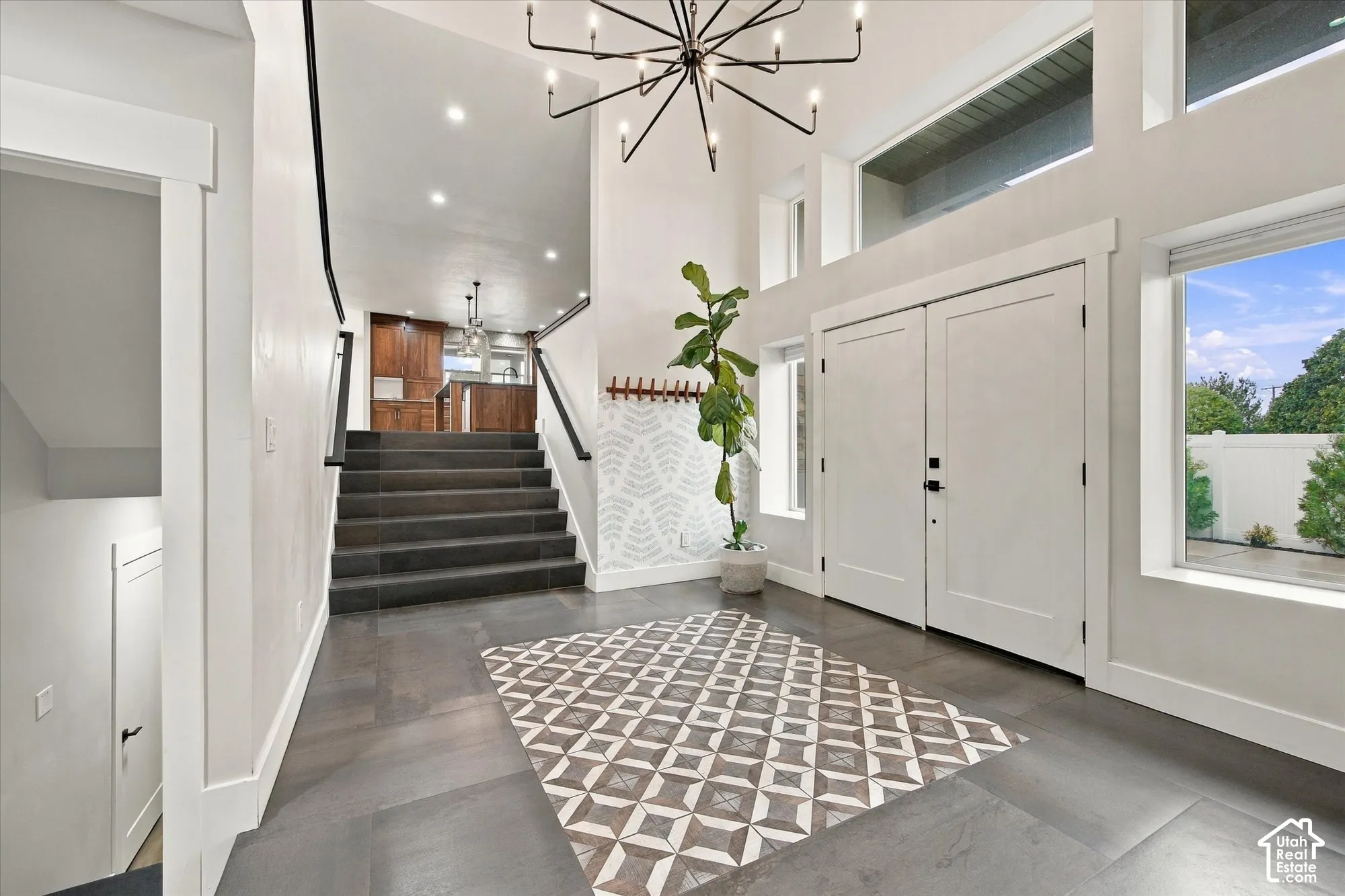 Double-door entryway featuring high ceilings, large multi-pane windows, a modern chandelier, and dark-toned tile flooring