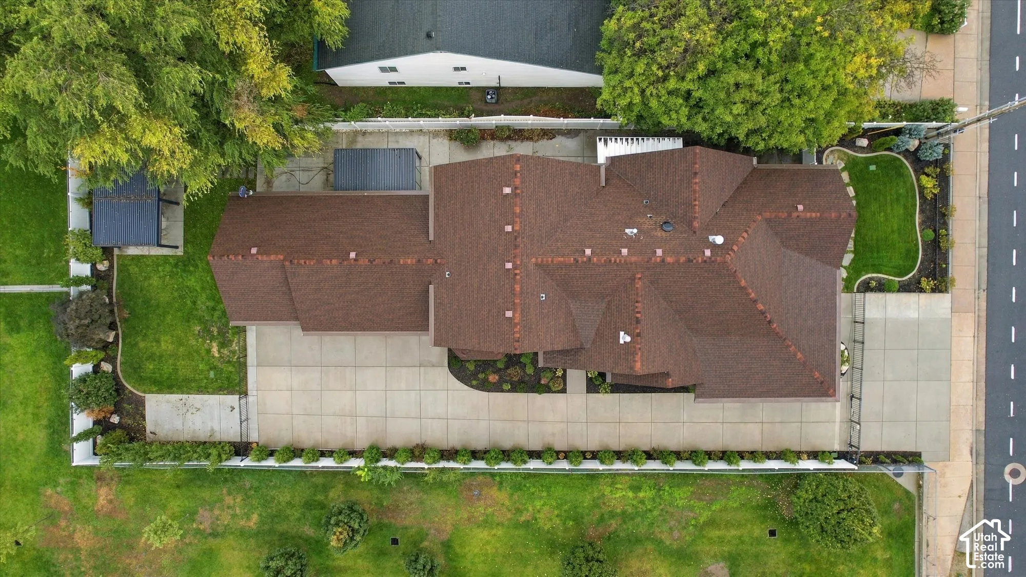 Aerial perspective featuring a multi-gabled roofline, concrete driveway, fenced perimeter, manicured lawn, and mature landscaping