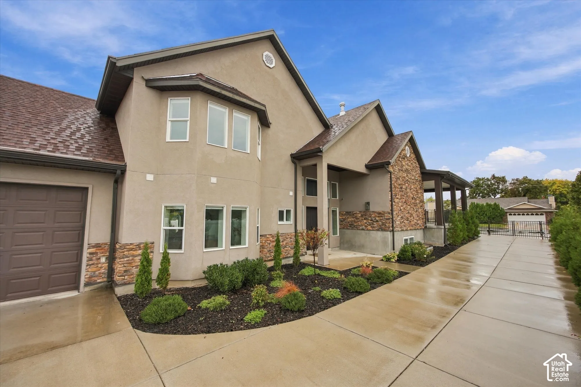 Stucco exterior featuring stacked stone accents, multi-gabled roofline, concrete driveway, and landscaped shrubbery