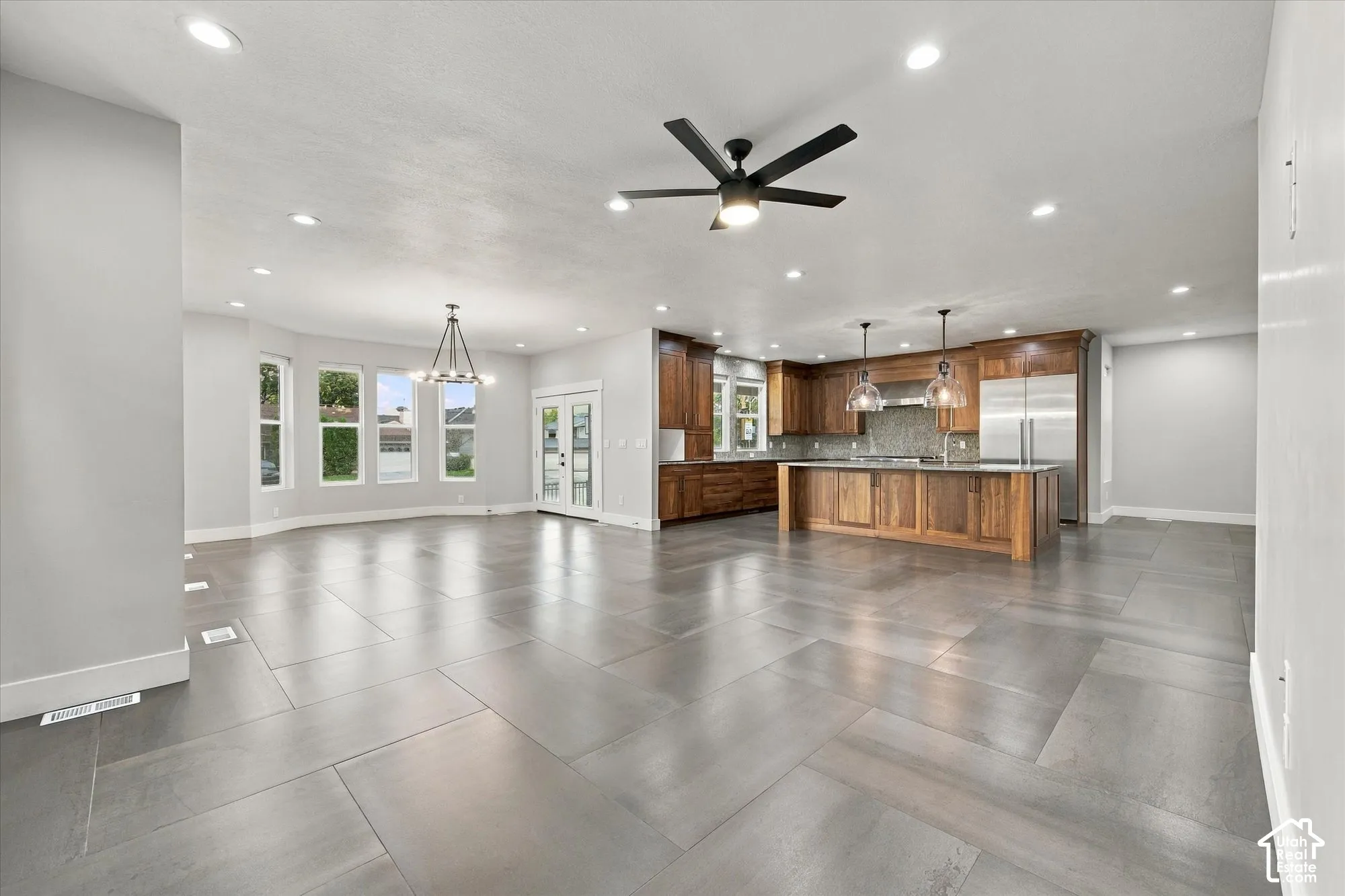 Open-concept interior featuring large-format tile flooring, a kitchen island with built-in cabinetry, recessed lighting, double-door exterior access, and a bay window