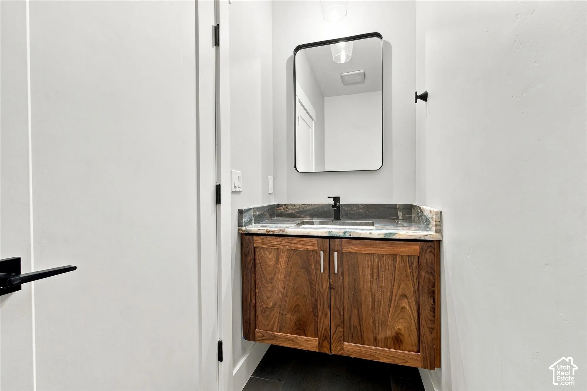 Floating vanity with wood-grain cabinetry, stone countertop, undermount sink, matte black faucet, and rectangular wall-mounted mirror