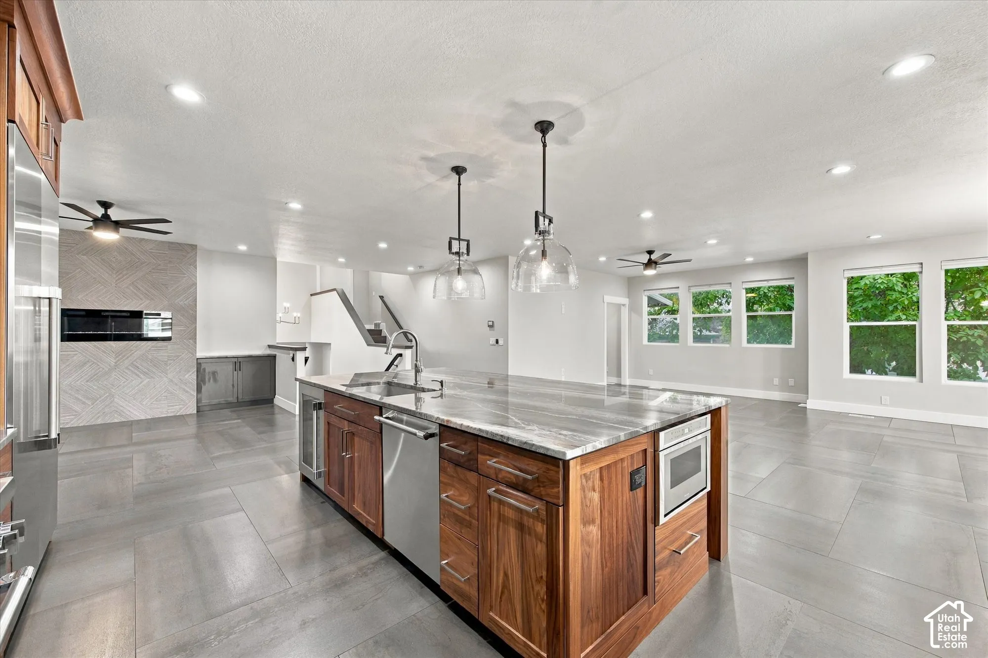 Kitchen featuring an oversized island with stone-finish countertops, warm-toned wood cabinetry, stainless steel appliances, geometric tile fireplace surround, and recessed lighting