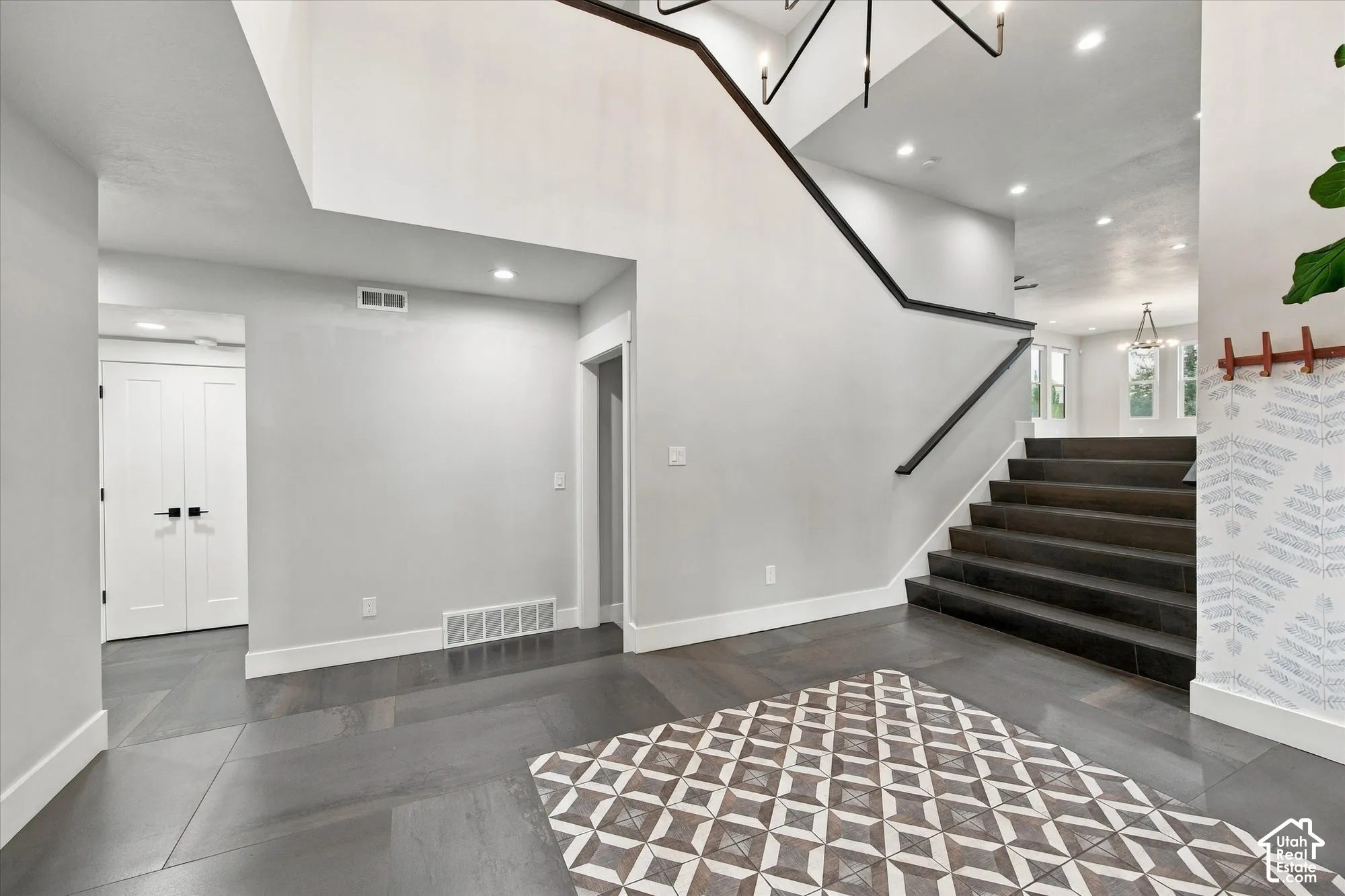 Entryway featuring dark-toned tile flooring, geometric tile inlay, staircase with dark wood-finish treads, and black iron handrail