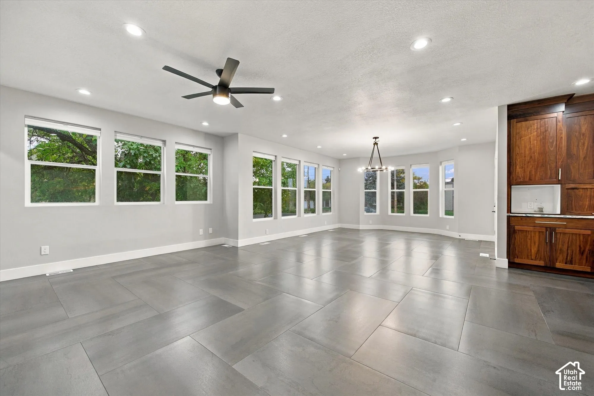 Spacious interior featuring large-format tile flooring, recessed lighting, a modern ceiling fan, multiple windows with grid detailing, and built-in wood cabinetry