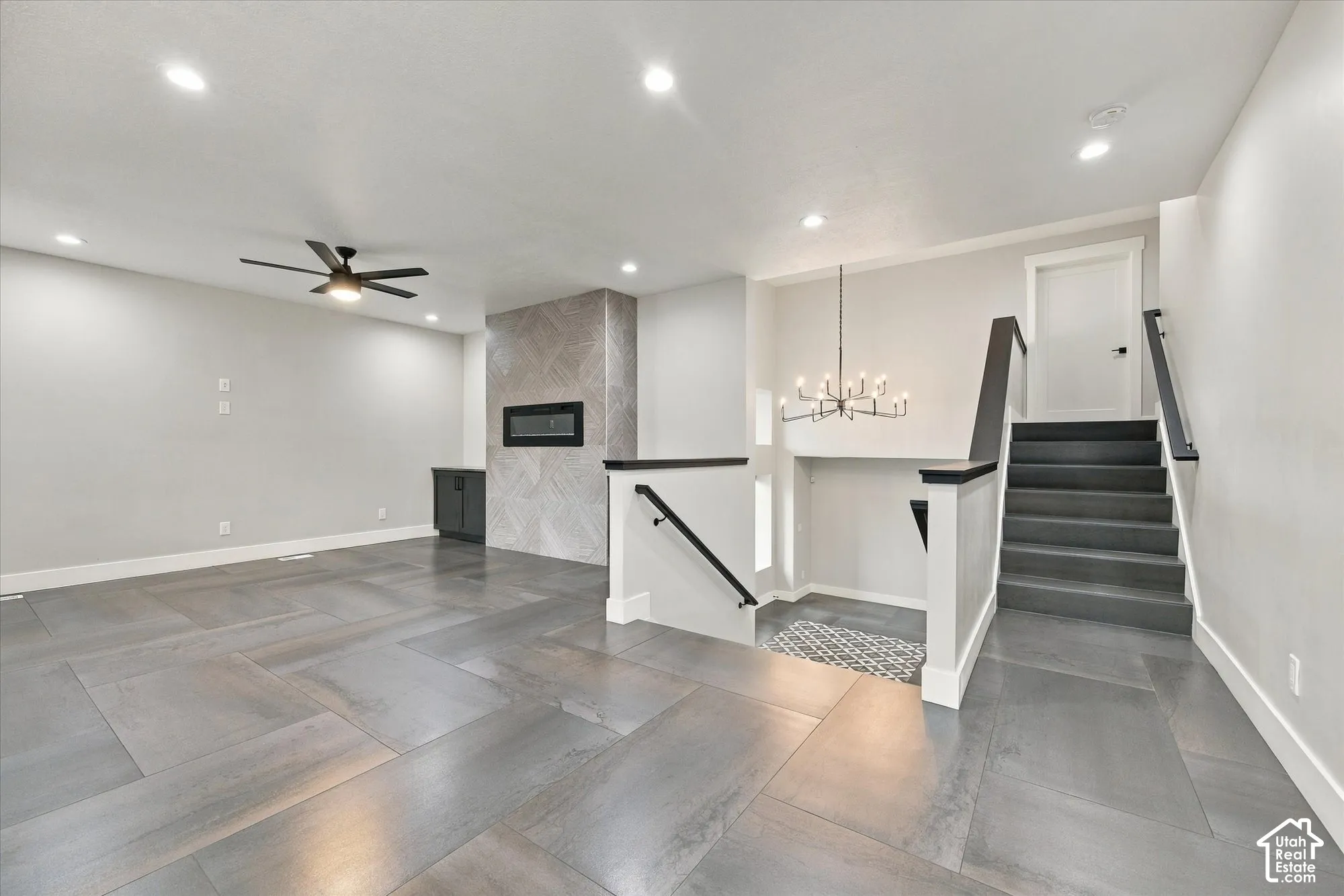 Large-format tile flooring, fireplace with a decorative tile surround, recessed lighting, multi-tiered chandelier, and staircase with a matte black handrail