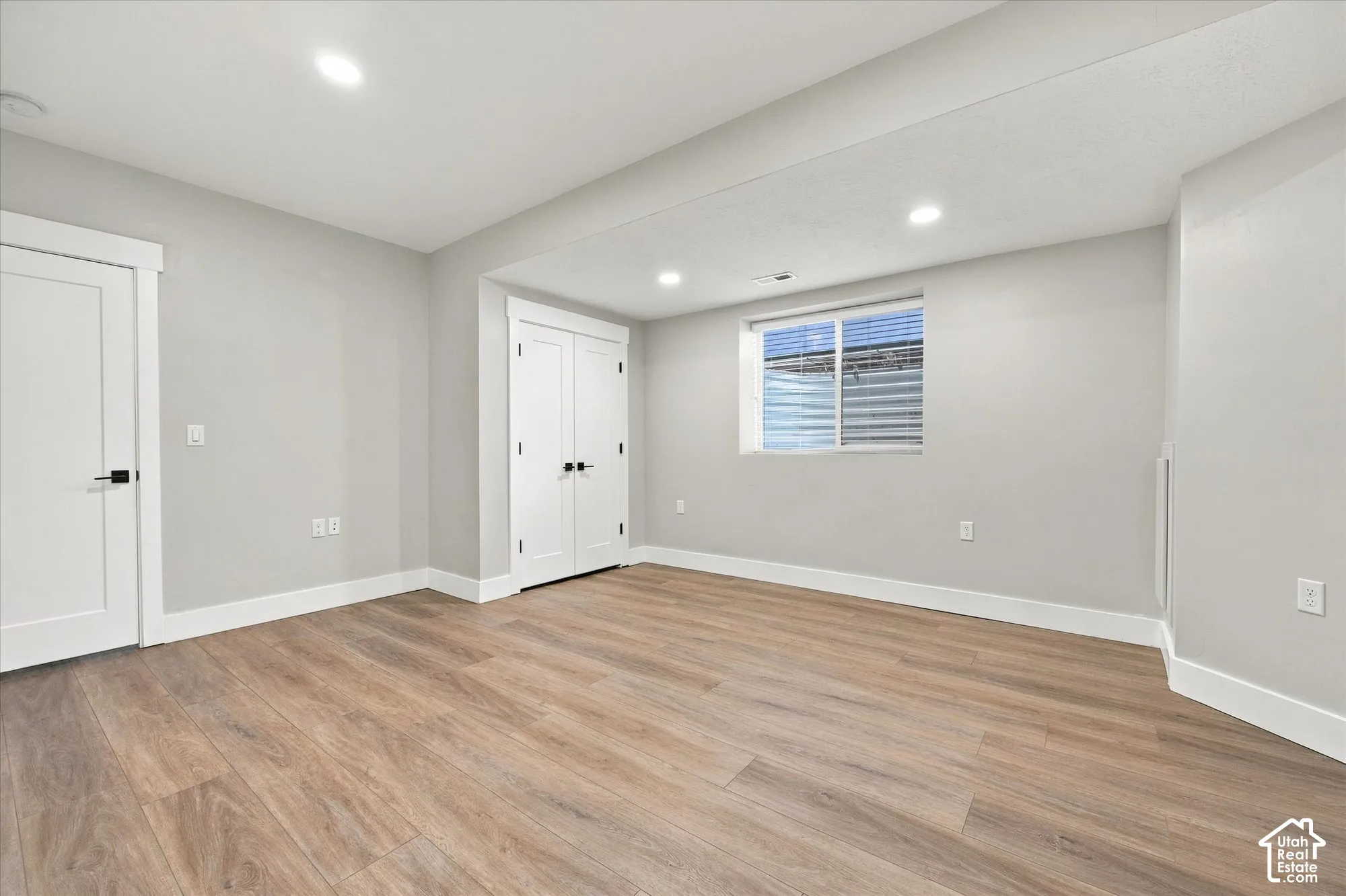 Neutral-toned interior featuring wood-finish flooring, recessed lighting, double-door closet with matte black hardware, and an egress window