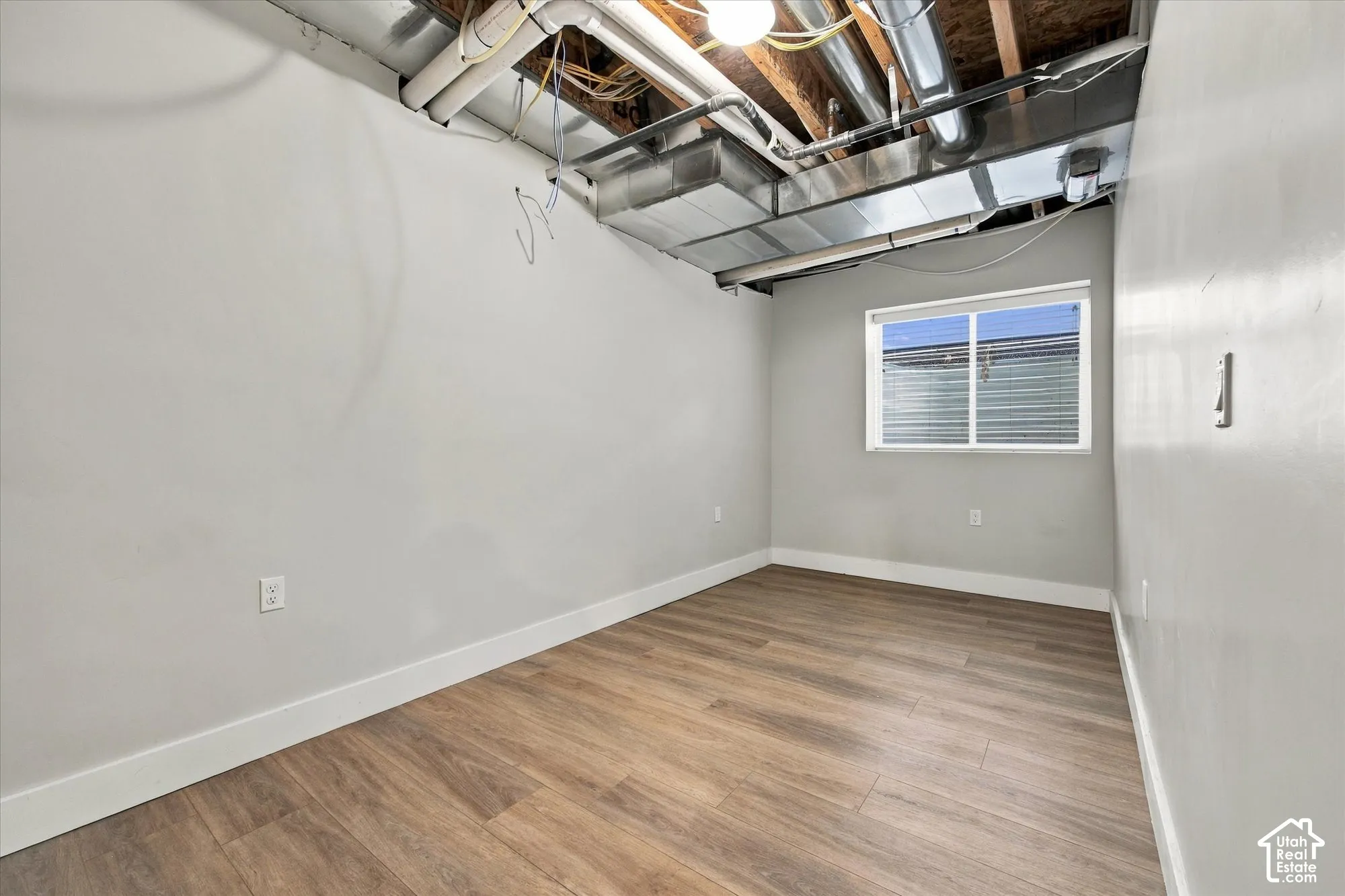 Room featuring wood-finish flooring, neutral wall paint, and a sliding window with exposed industrial ceiling ductwork