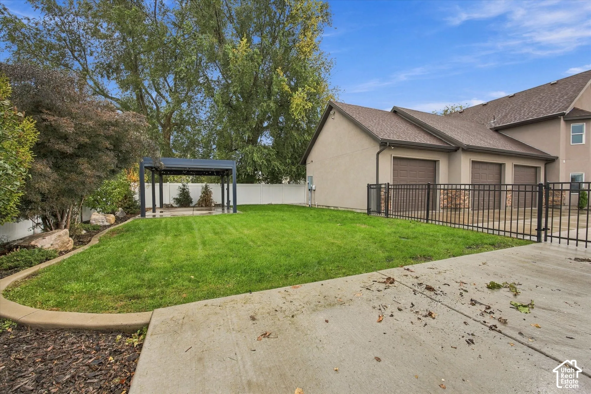 Fenced backyard featuring a manicured lawn, metal pergola, concrete hardscaping, and mature trees