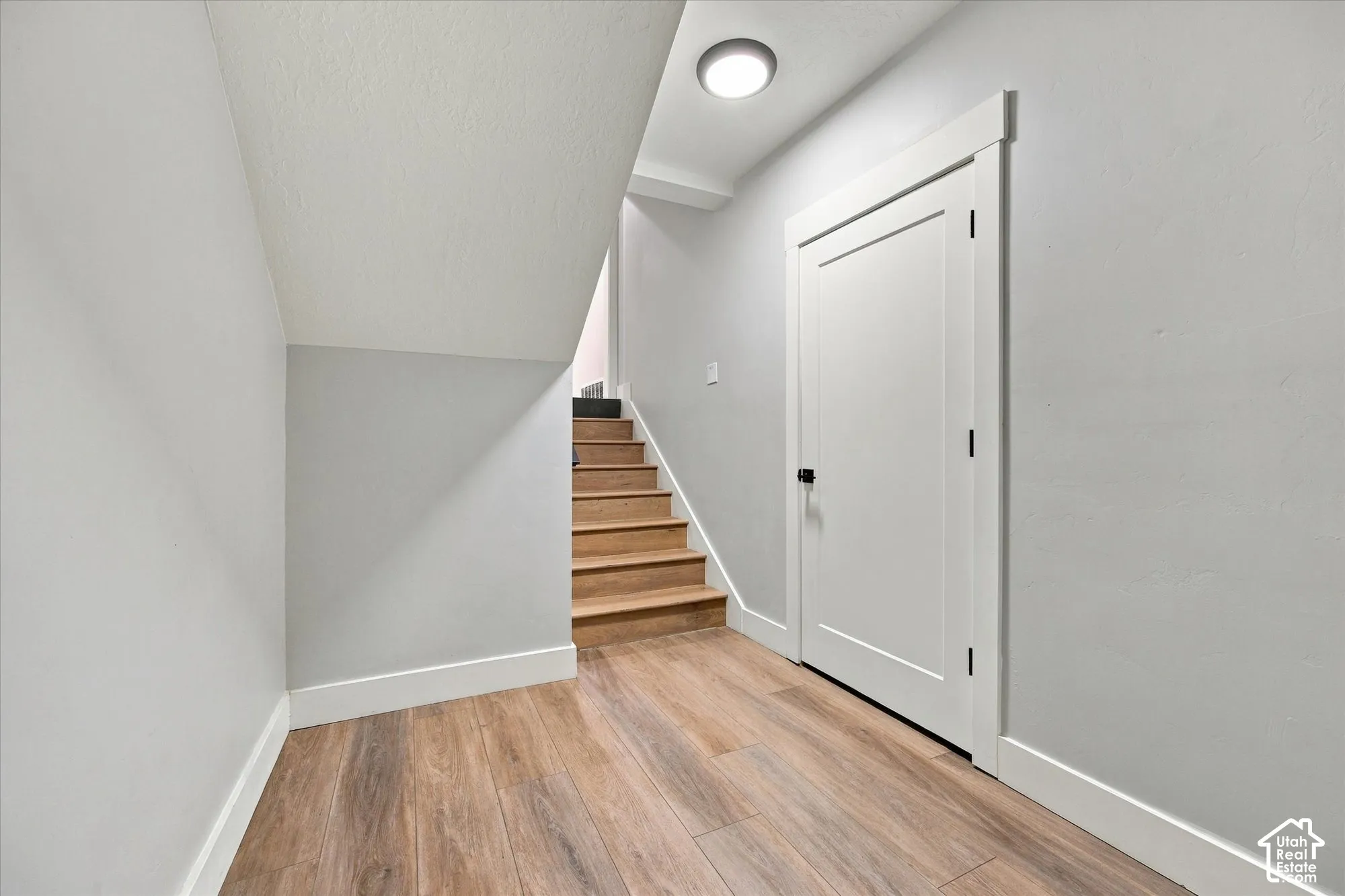 Wood-finish flooring, shaker-style interior door with matte black hardware, and wood-tread staircase