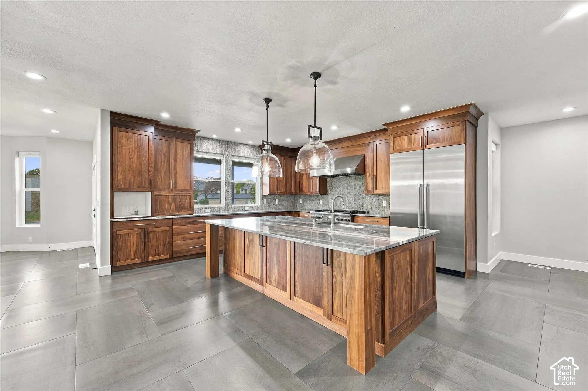 Kitchen featuring stained wood cabinetry, central island with stone countertop, stainless steel refrigerator, recessed lighting, and large-format tile flooring
