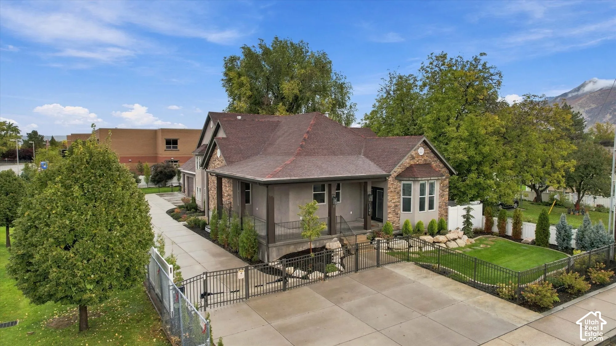 Single-story exterior featuring a stone and siding facade, a wrap-around covered porch, a concrete driveway with gated entry, and professional landscaping