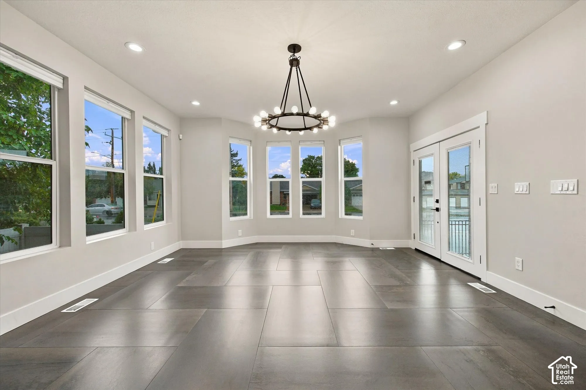 Spacious room featuring large-format tile flooring, a multi-light wagon wheel chandelier, recessed lighting, expansive windows, and double glass-pane doors