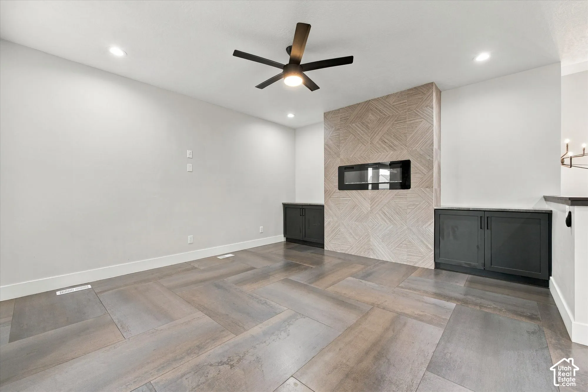 Room featuring wood-finish flooring in a herringbone pattern, a fireplace with geometric-tiled surround, built-in cabinetry, and a ceiling fan with integrated lighting