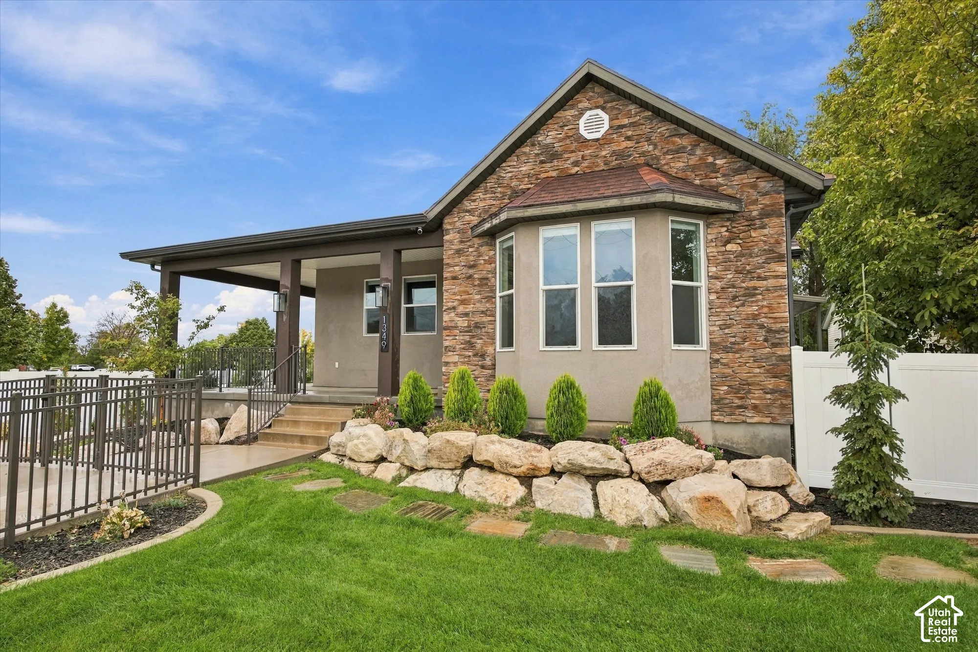Exterior featuring stacked stone facade, covered porch with dark-tone structural columns, bay window, and tiered boulder landscaping