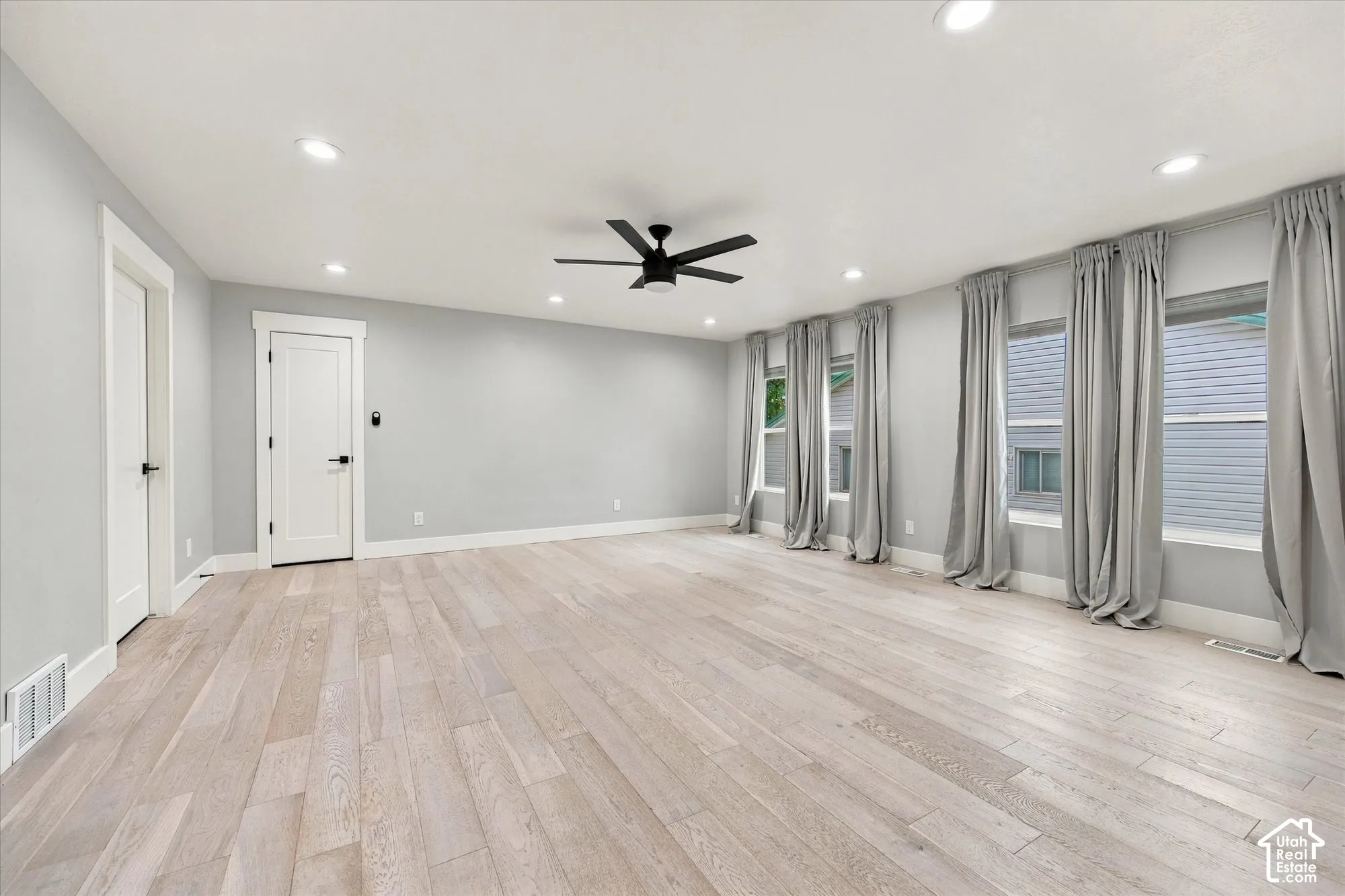 Spacious room featuring wood-finish flooring, recessed lighting, a modern ceiling fan, and large windows