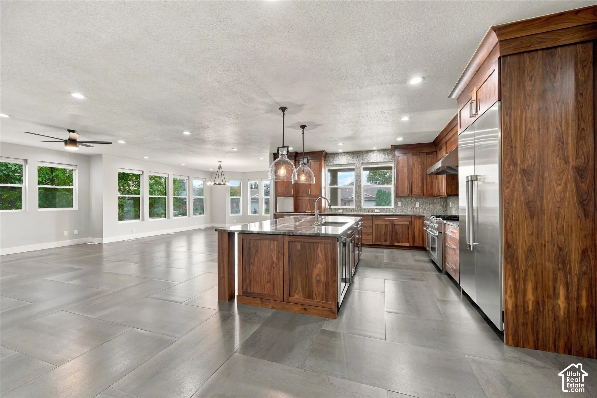 Kitchen featuring wood cabinetry, stone countertops, central island with pendant lighting, stainless steel appliances, and large-format tile flooring