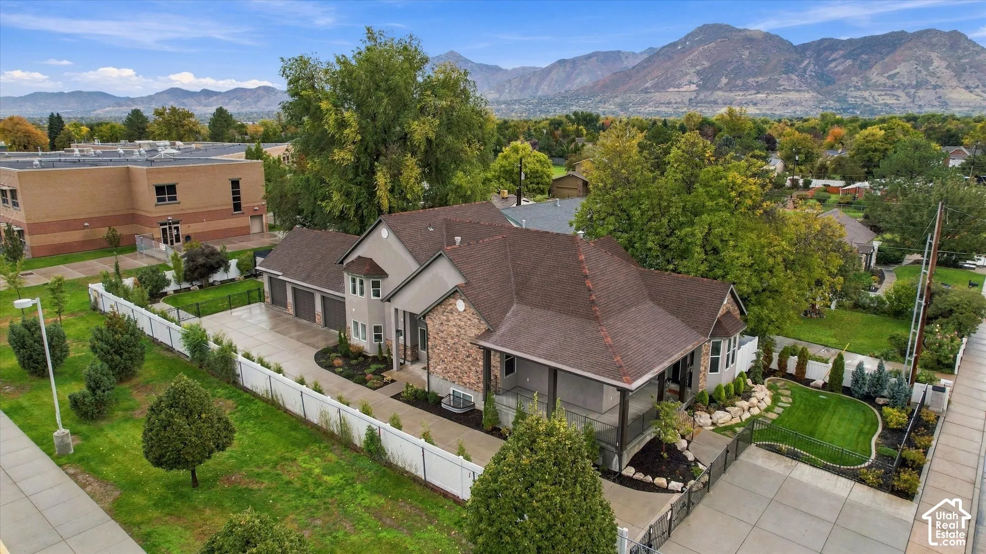 Multi-level residence featuring a stone and siding exterior, multi-car garage, covered porch, fenced landscaping, and mountain backdrop