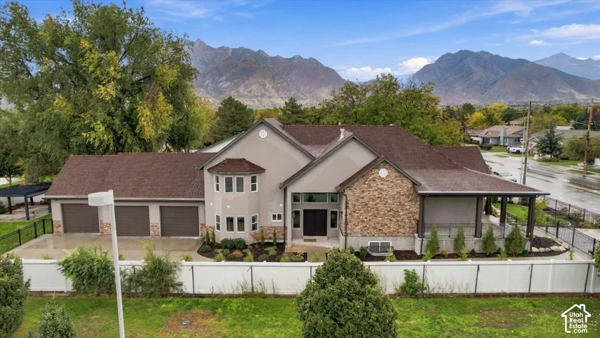Exterior facade featuring stone veneer detailing, a three-car garage, covered patio space, and prominent mountain backdrop
