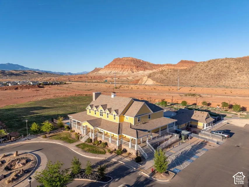 Multi-level structure featuring a wraparound porch, exterior chimney, shingle roofing, and surface parking lot, set against a mountainous backdrop