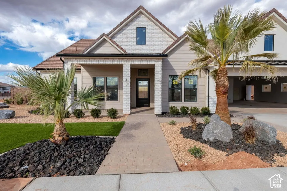 Single-story residence featuring a white brick and horizontal siding exterior, dual-gabled roofline, paver stone walkway, and an attached garage