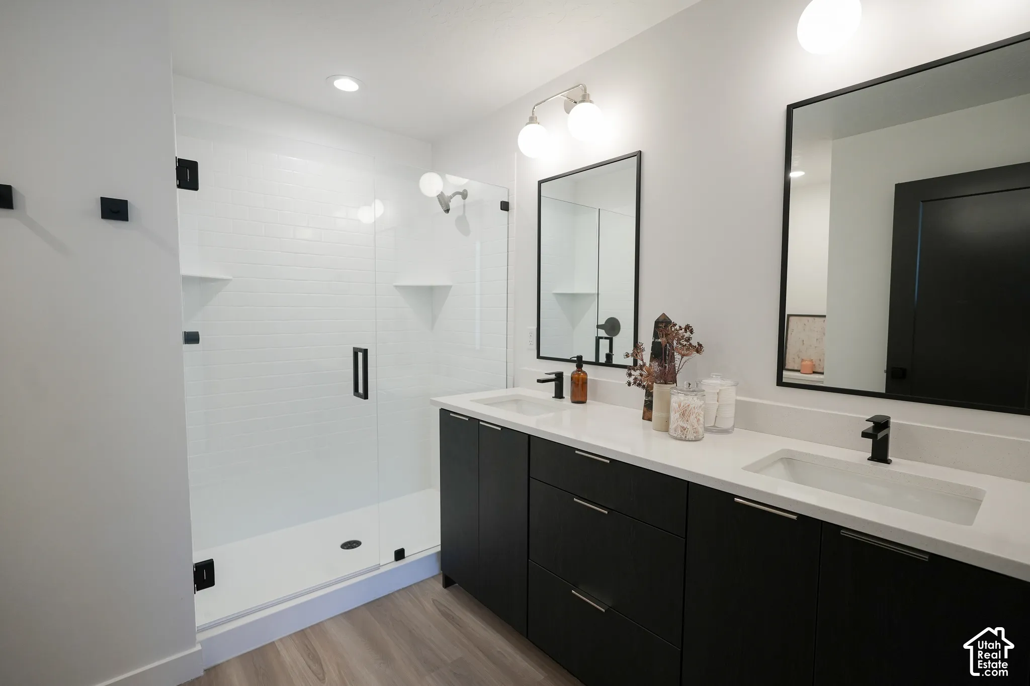 Dual-vanity cabinetry with dark finish, stone-surface countertops, under-mount sinks, matte black fixtures, and walk-in shower with frameless glass enclosure