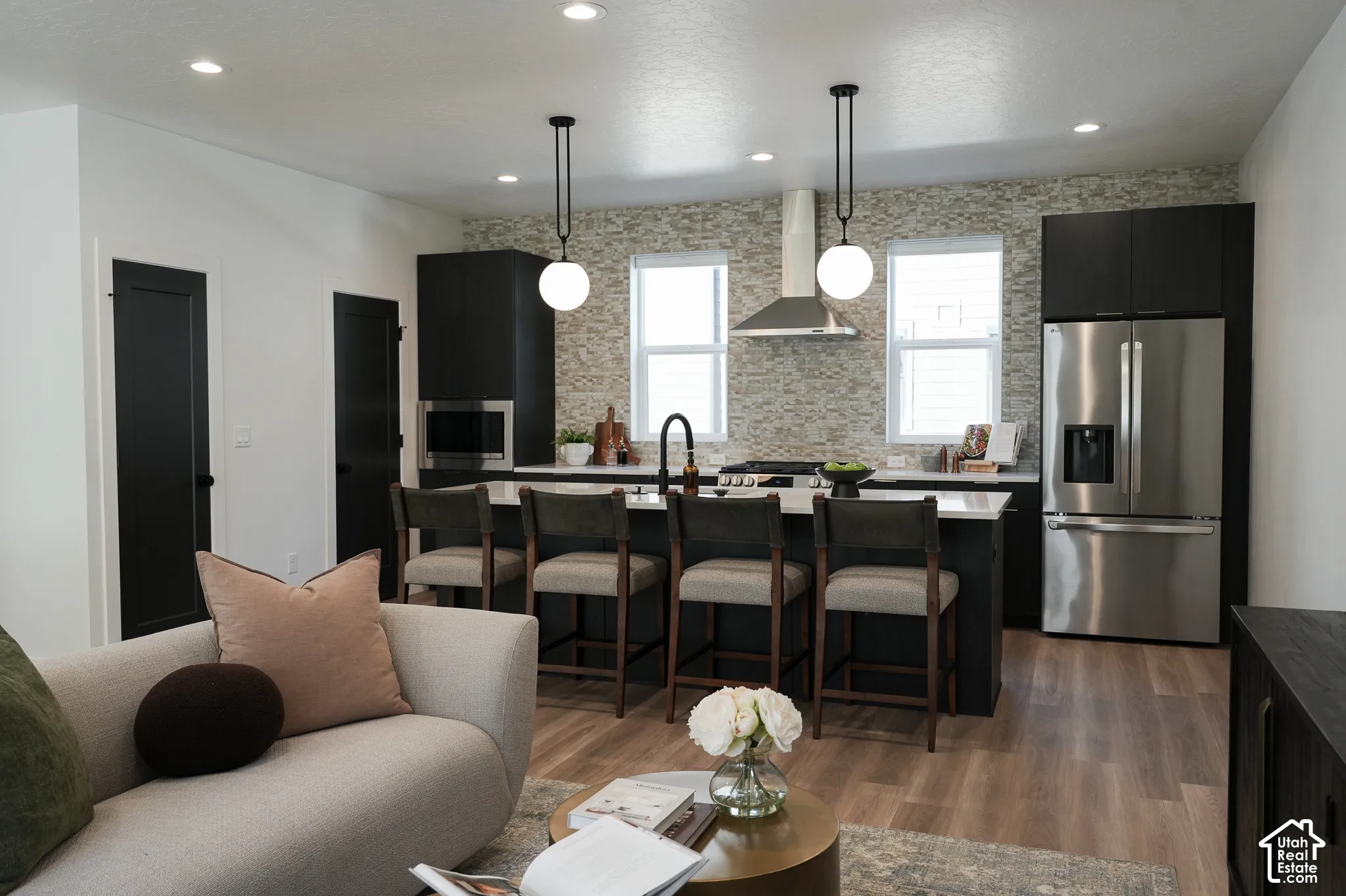 Kitchen featuring dark cabinetry, stone-style backsplash, stainless steel appliances, quartz-surface island, and globe pendant lighting