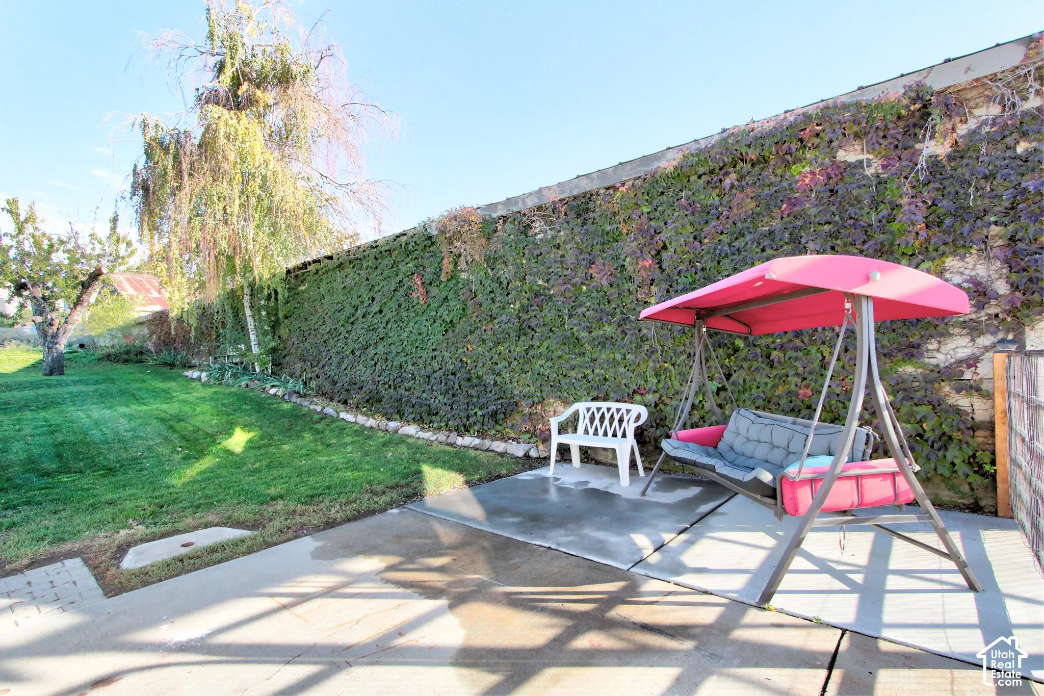 Concrete patio featuring a large stone perimeter wall adorned with climbing vegetation and a manicured lawn