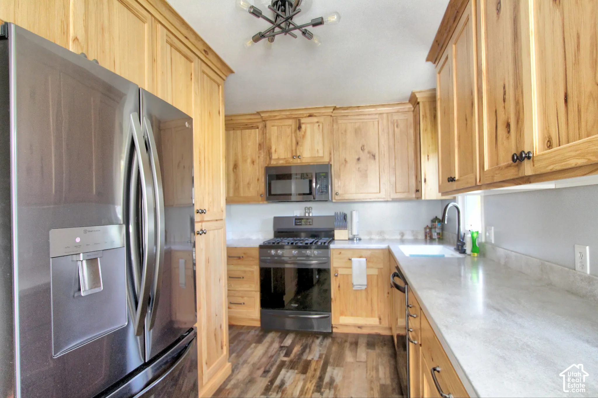 Kitchen featuring natural finish cabinetry, light-toned countertops, premium stainless steel appliances, wood-finish flooring, and multi-arm industrial-style ceiling lighting