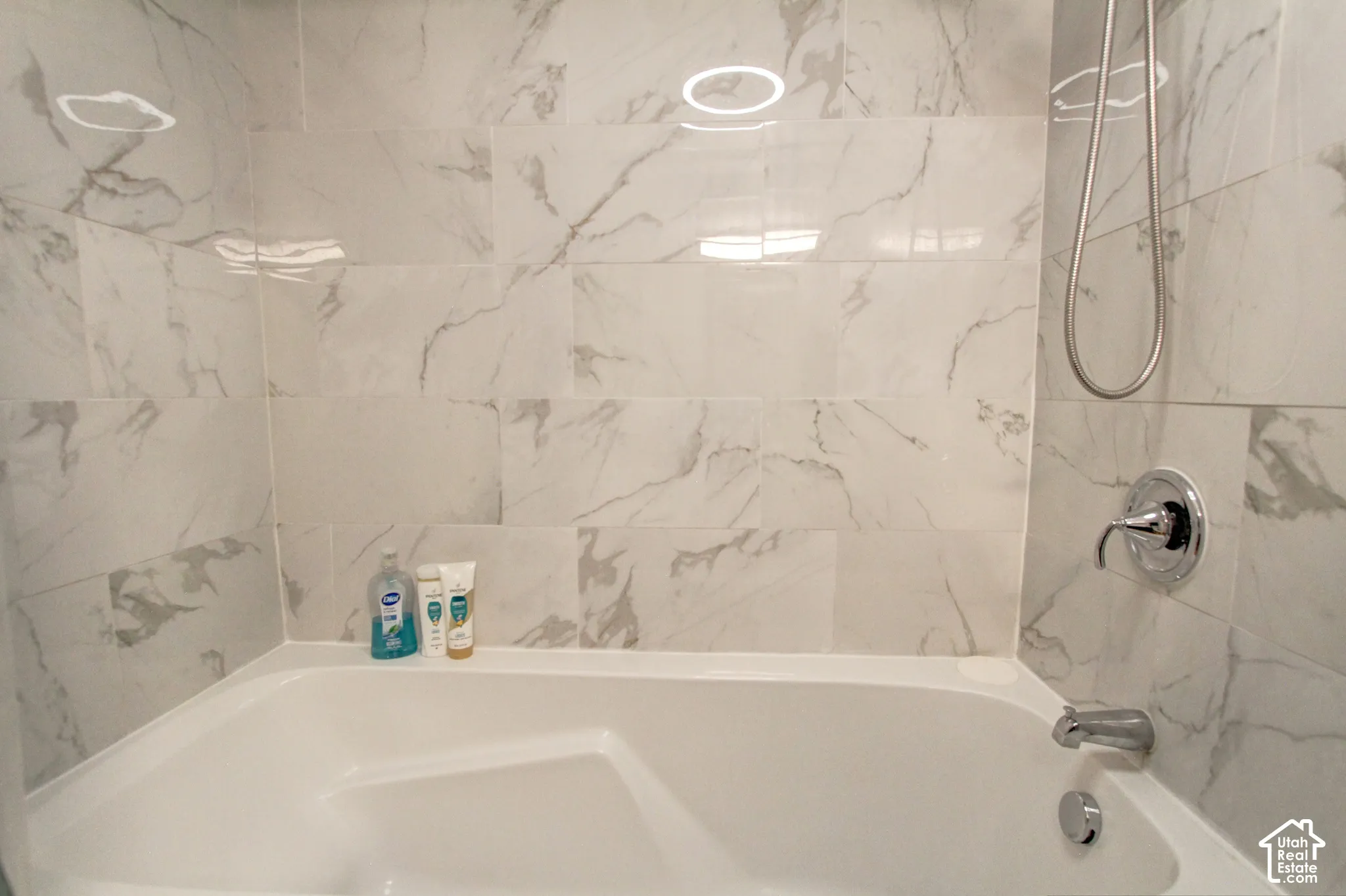 Deep soaking tub featuring large-format stone-finish wall tile, polished chrome hardware, and an adjustable handheld shower fixture