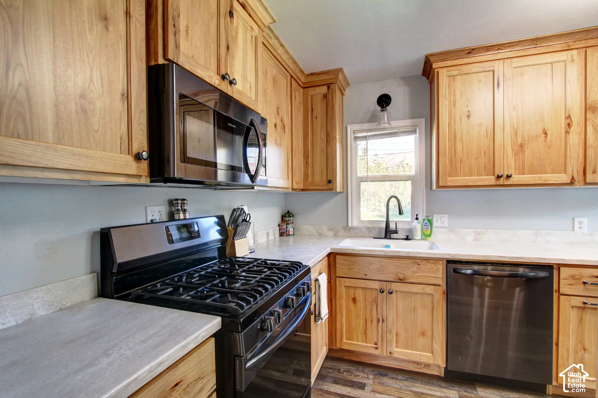 Kitchen featuring natural wood cabinetry, stone-finish countertops, premium black finish appliances, a white farmhouse-style sink with a high-arch faucet, and wood-finish flooring