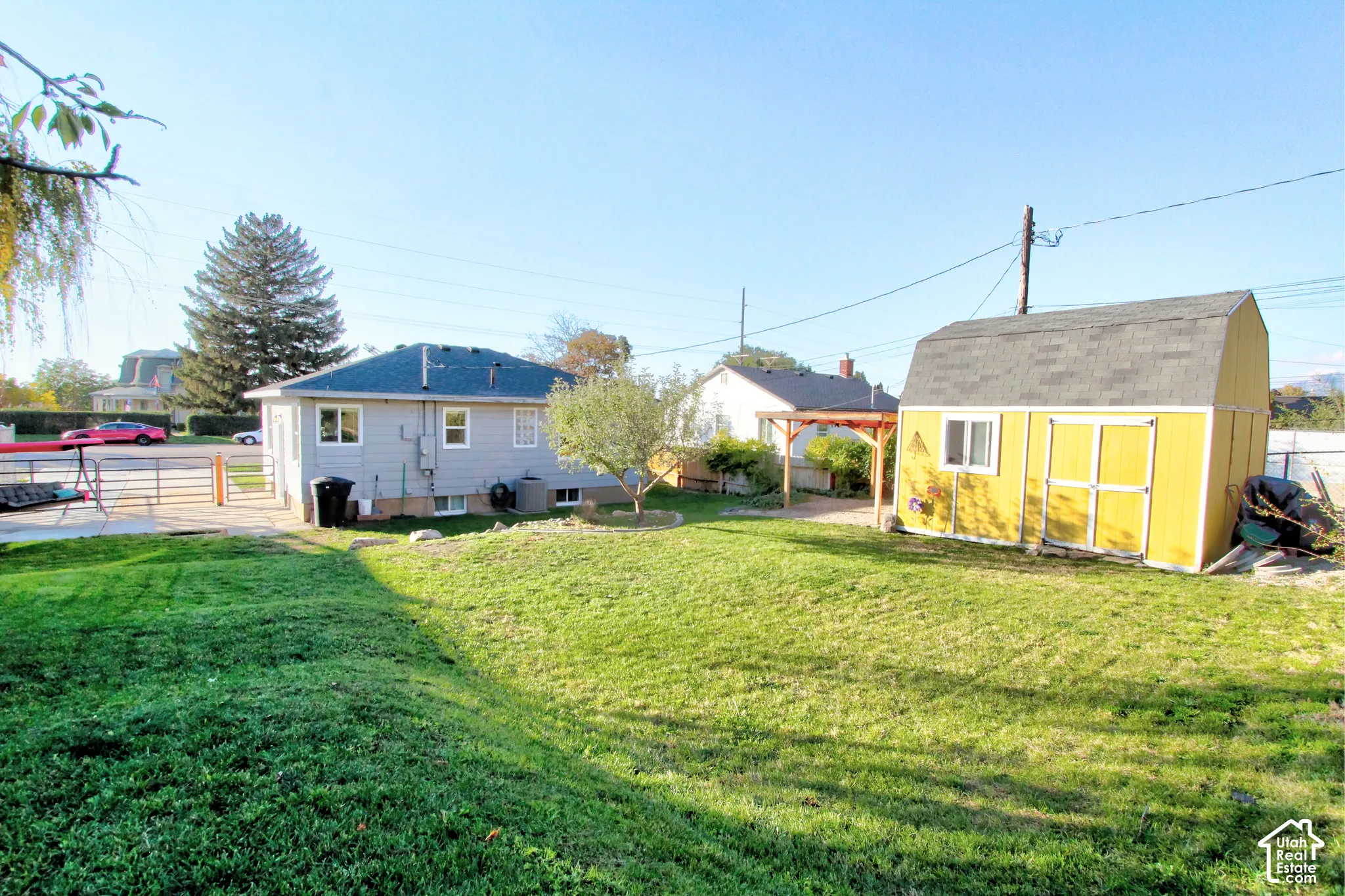 Expansive backyard featuring a manicured lawn, detached storage structure, wooden pergola, and perimeter fencing